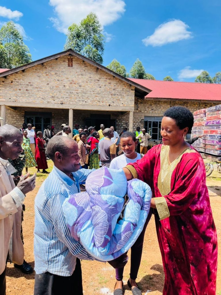 Loice Natukunda hands a new mattress and bedding to an elderly man
