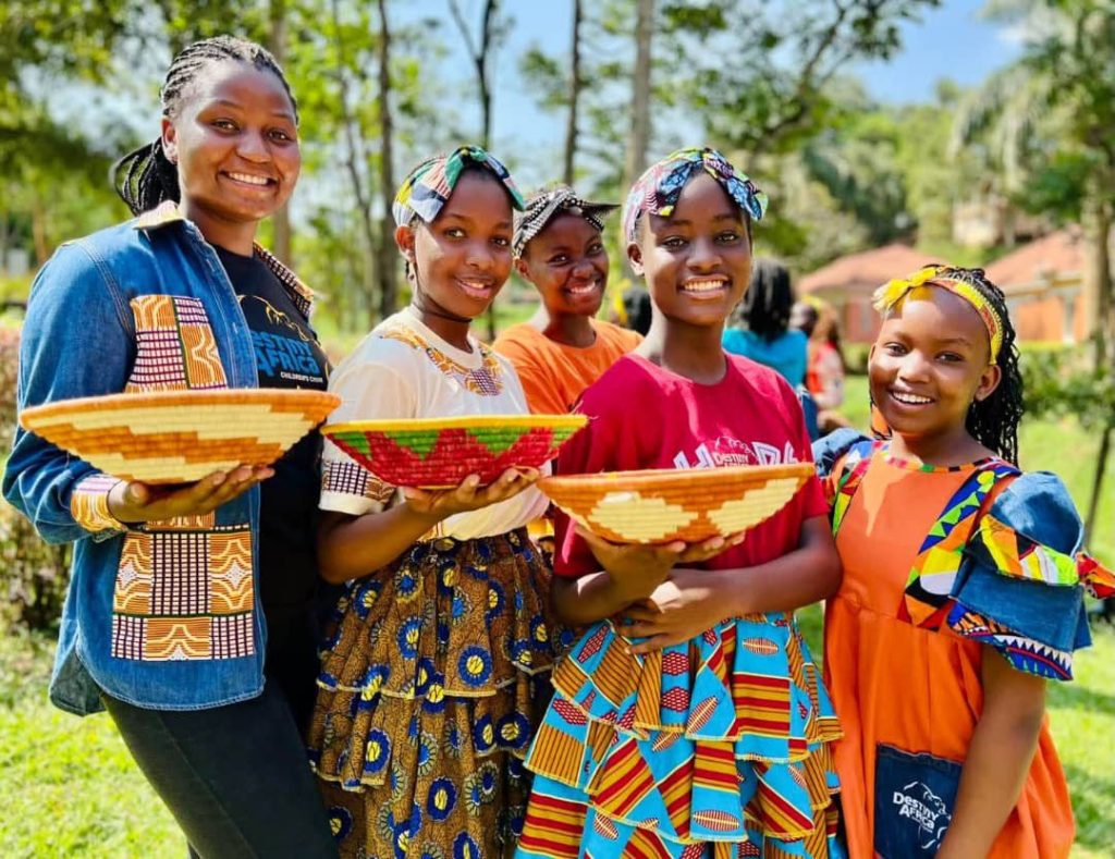 Girls in bright dresses carry woven baskets at the Elevate Her Uganda launch in Mitooma