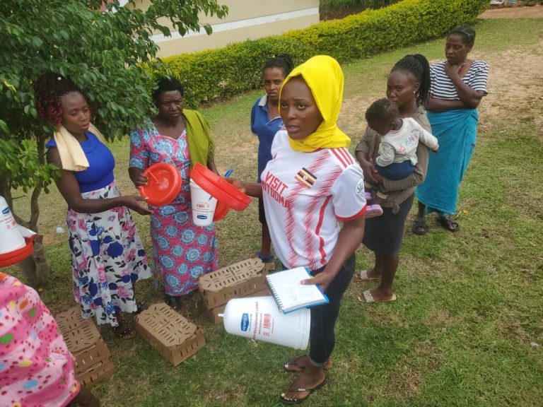 A woman carries poultry equipment across a field