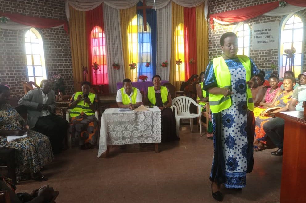 A woman in a high-visibility vest speaks to women seated in a church